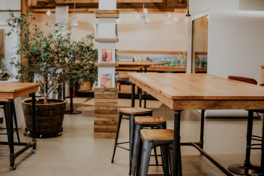 Mesa larga de madera con taburetes metálicos en un ambiente de oficina con plantas y decoración cálida